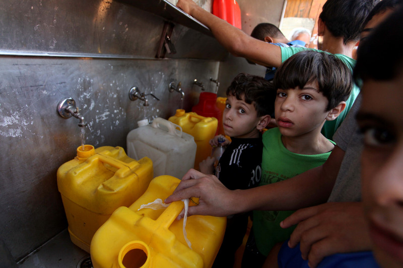Palestinians children fill plastic bottles and water containers with drinking water from a public tap in Jabalia in the northern Gaza Strip on July 27, 2014. Three Palestinians were killed in shelling as the Israeli military resumed its assault on Gaza after Hamas shunned an extended lull accepted by Israel, medics said. Photo by Ashraf Amra